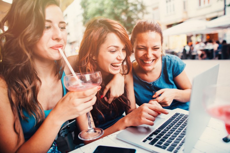 Três mulheres reunidas, se divertindo enquanto veem algo no computador