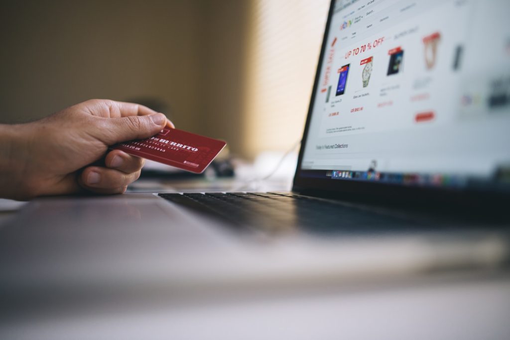 Experiência de compra: computador em um site de e-commerce e, à esquerda, uma mão segurando um cartão de crédito.