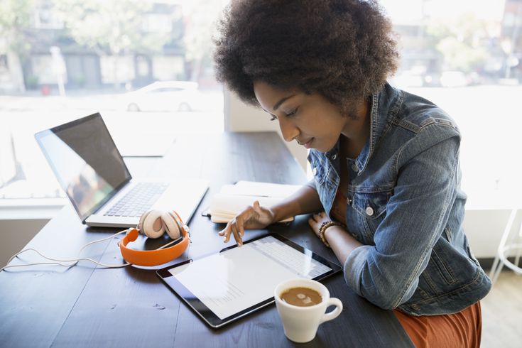 Mulher negra sentada a mesa, lendo no iPad. À sua esquerda, uma xícara de café. À sua direita, um notebook e um fone de ouvido laranja. A mulher veste uma jaqueta jeans e uma saia laranja.  O que é filtro web?