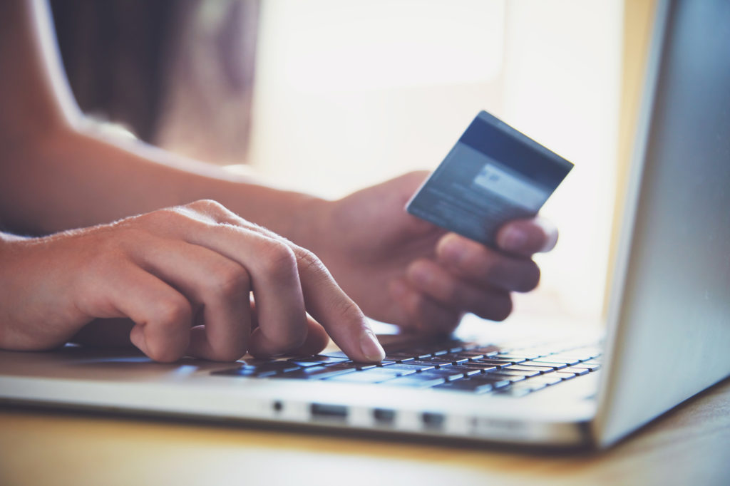 Pagamento dos clientes: pessoa digitando no computador, com um cartão de crédito na mão.