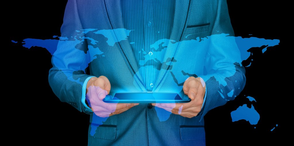 Pequenas e médias empresas: Homem de terno azul, com imagem sobreposta do mapa-múndi, segura um tablet entre as mãos.