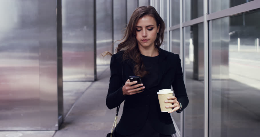 Mulher de negócios olha o smarphone enquanto caminha com café na mão