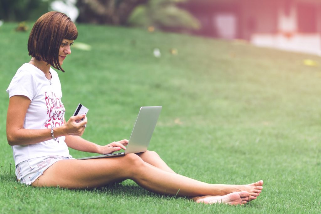 Novos Clientes: mulher sentada na grama fazendo compras em uma loja online.