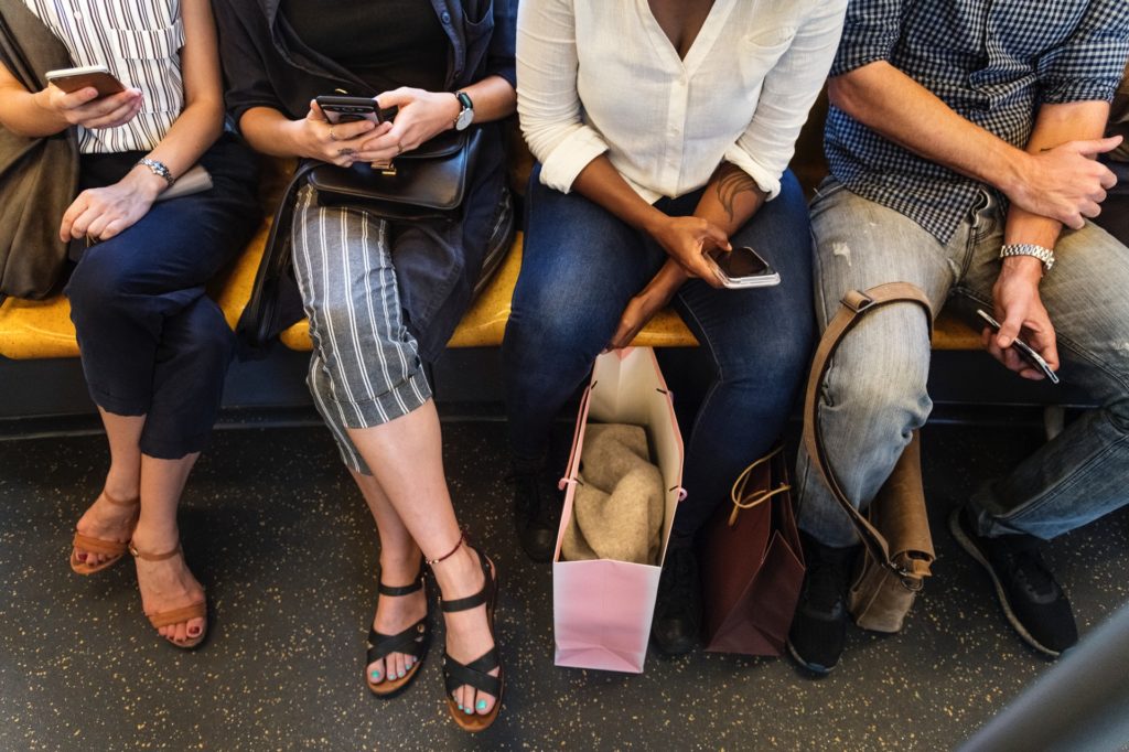 Era mobile: grupo sentado no metrô. Todos estão mexendo no celular.
