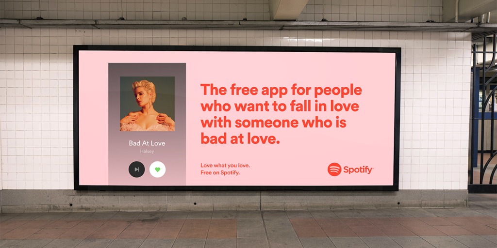Imagem de um outdoor do Spotify em uma estação de metrô. No outdoor, a seguinte mensagem "o aplicativo gratuito para quem deseja se apaixonar por alguém que é ruim no amor". Ao lado da mensagem, um print do spotify tocando a música "Bad At Love" (ruim no amor) da cantora Halsey.