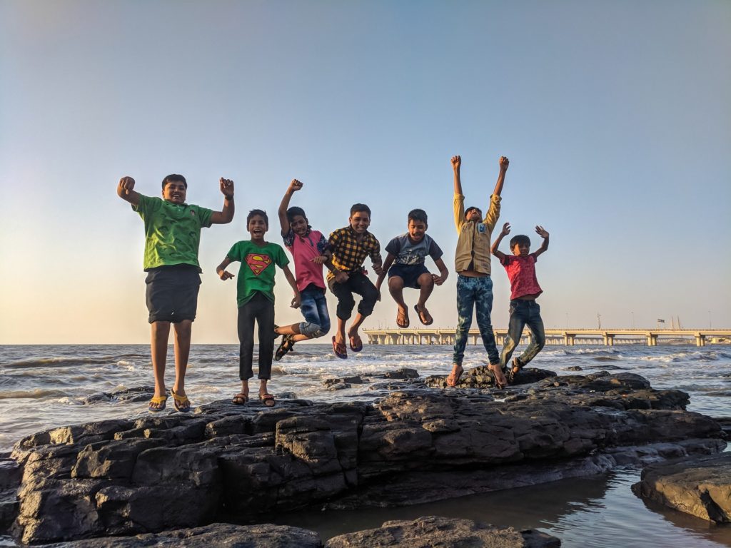 Geração Z: grupo de sete meninos pulando sobre as pedras de uma praia.
