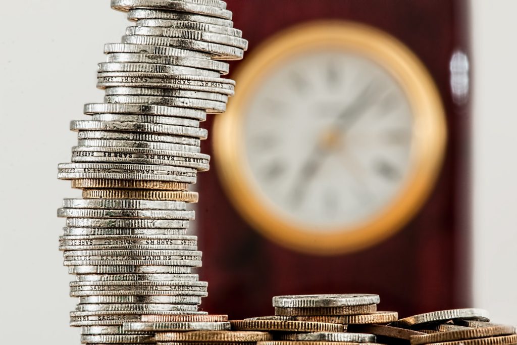 controle financeiro empresarial: pilha de moedas e um relógio atrás