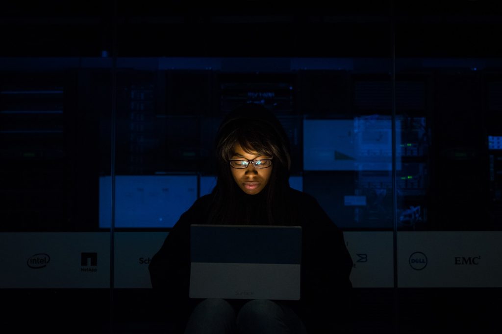 Mulher iluminada pela luz de um computador, em um local escuro