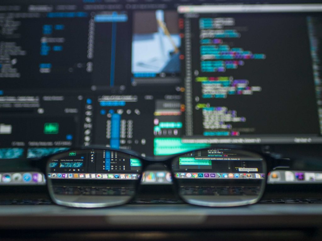 óculos de grau colocado em frente a um computador, que tem, em sua tela, diversos códigos.