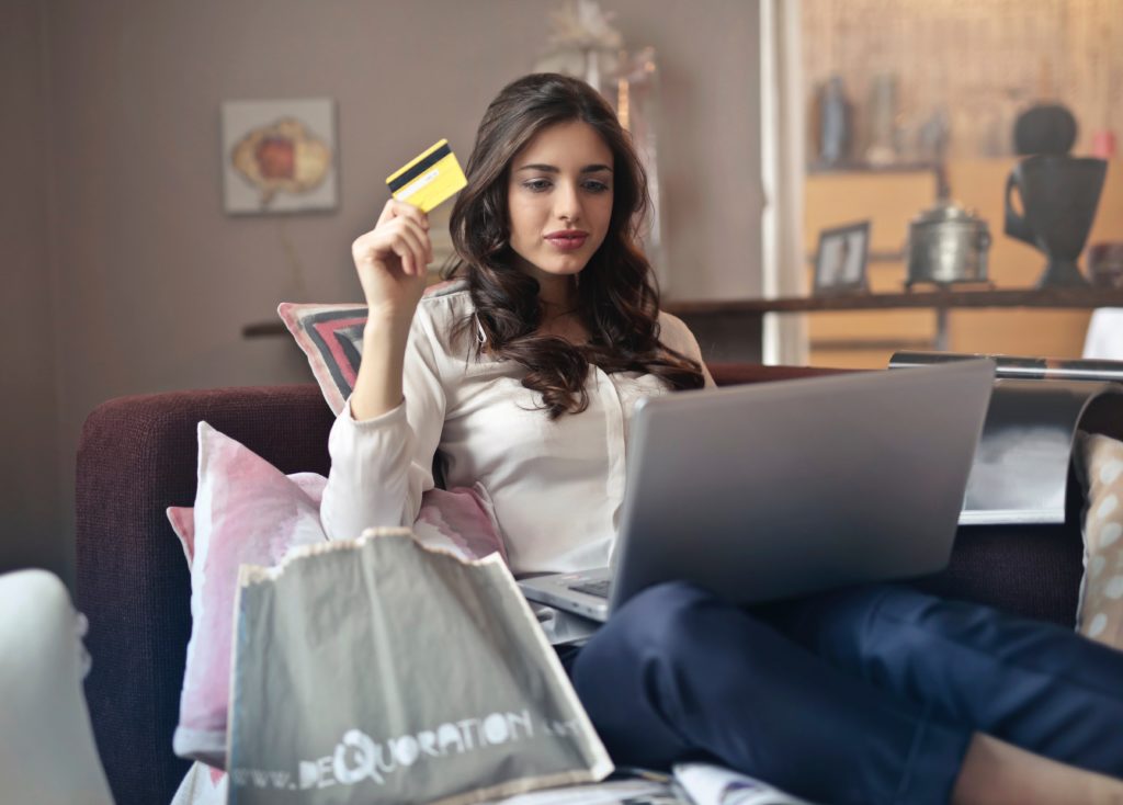 Preço em tempo real: mulher sentada com um computador no colo segurando um cartão de crédito.