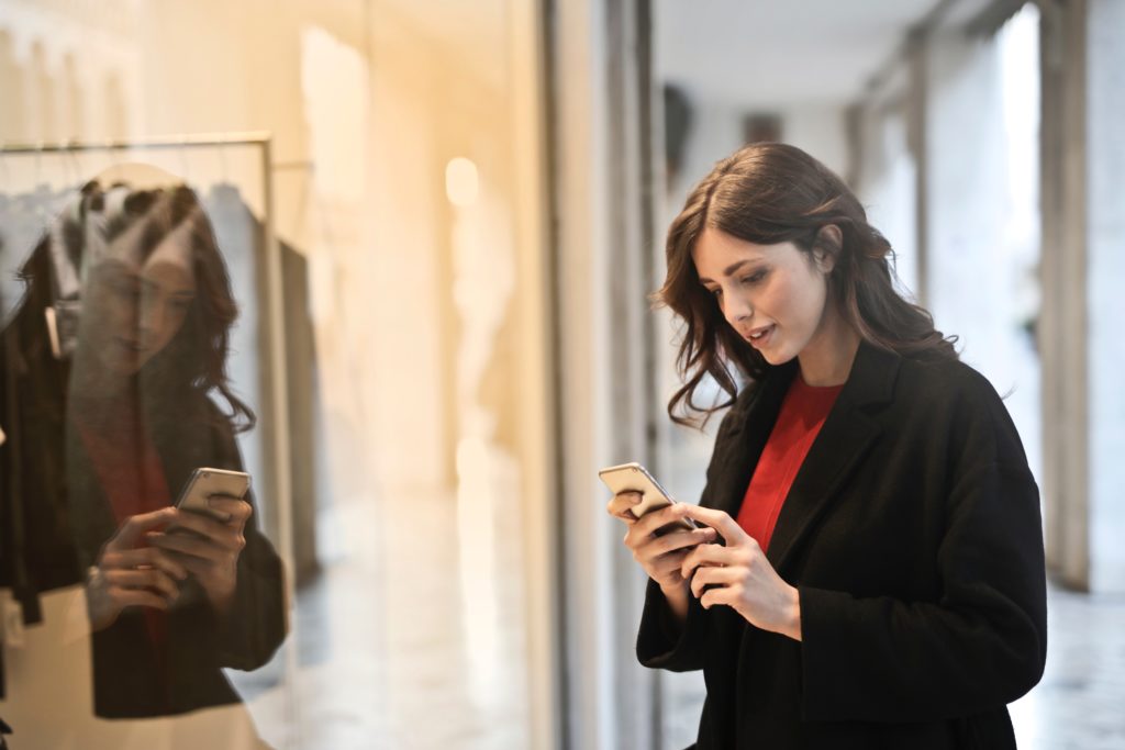 Preço em tempo real: mulher segurando um celular em frente a uma vitrine