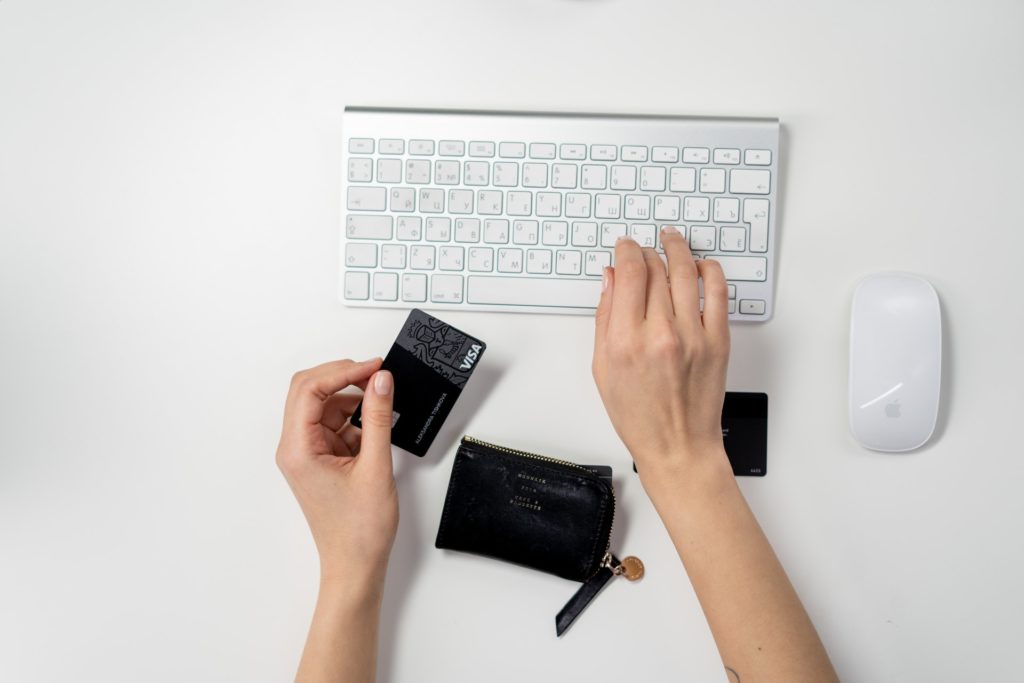 Imagem de um teclado e uma pessoa com um cartão de crédito nas mãos digitando. 