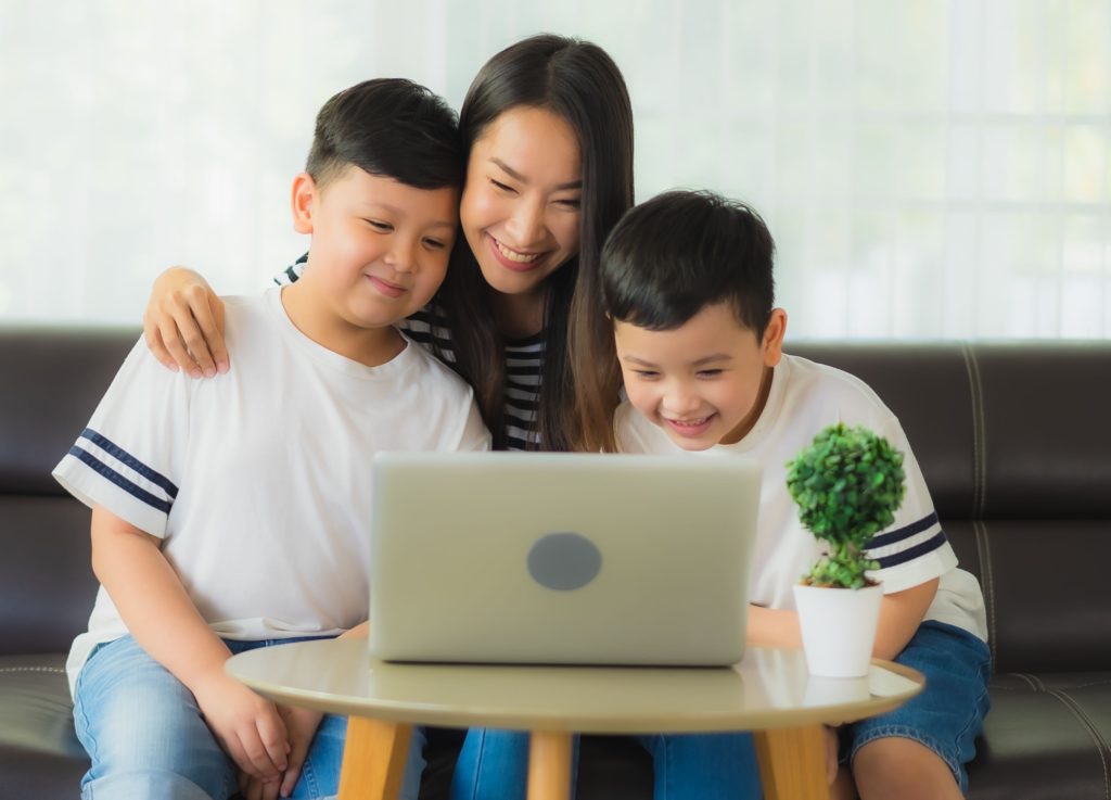 Imagem de uma mulher sorrindo com seus dois filhos assistindo algo no notebook para simbolizar a digitalização na educação. 