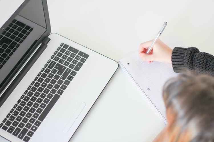 aulas online: imagem de uma pessoa escrevendo em um caderno e um computador em frente dela. 
