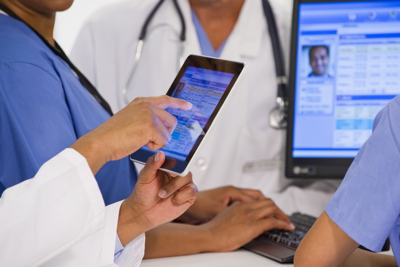 Imagem de médicos e enfermeiros com um tablet na mão  consultando o prontuário médico de um paciente. 