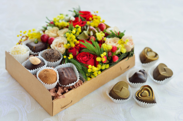 Imagem de uma caixa de bombons com flores dentro dela. 