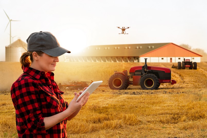 Um agricultor com tablet controla tratores autônomos e drone em uma fazenda inteligente.