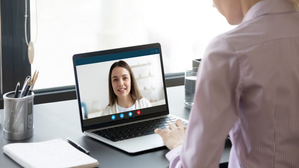 Imagem de uma mulher sentada na frente de um computador conversando uma pessoa em uma videochamada para simbolizar a terapia online