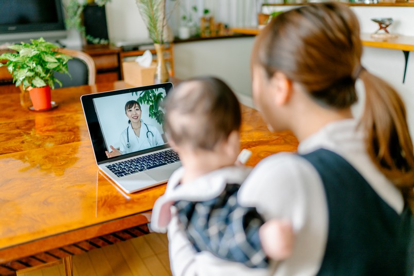 Imagem de uma pediatra online pelo computador e de uma mãe segurando um bebê na frente da tela. 