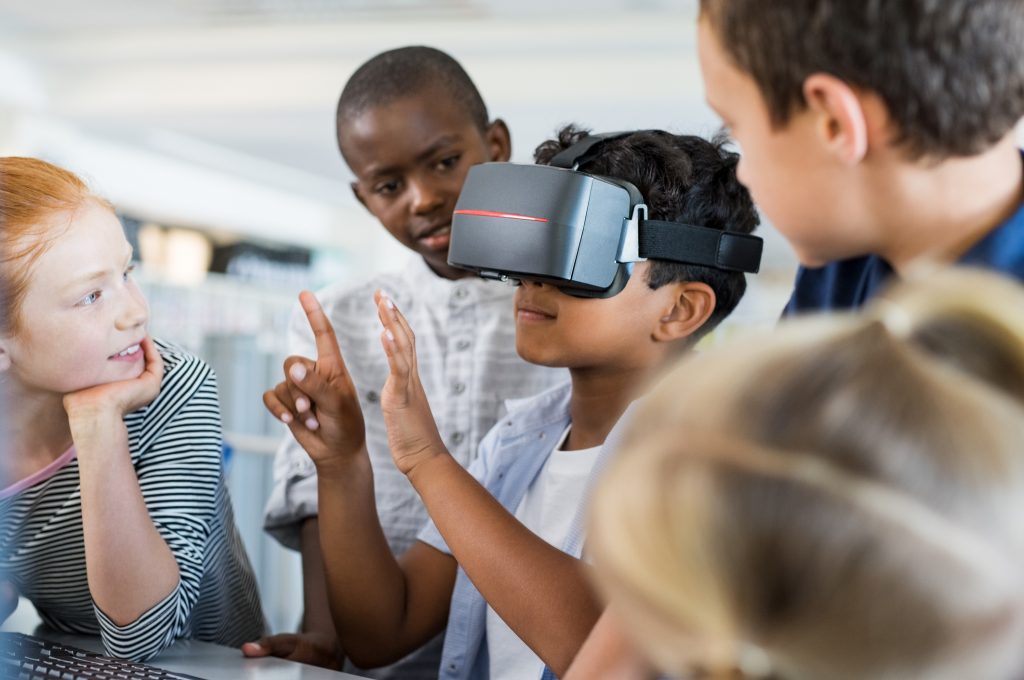Criança com headset de realidade virtual junto a outras crianças no ensino híbrido