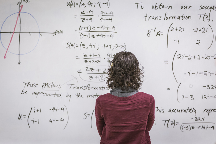 Fotografia de uma mulher de costas olhando para um quadro com anotações matemáticas