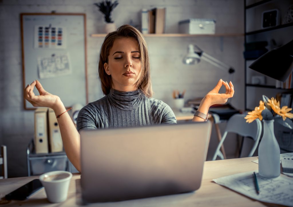 Mulher meditando em frente ao computador, representando o bem estar no trabalho