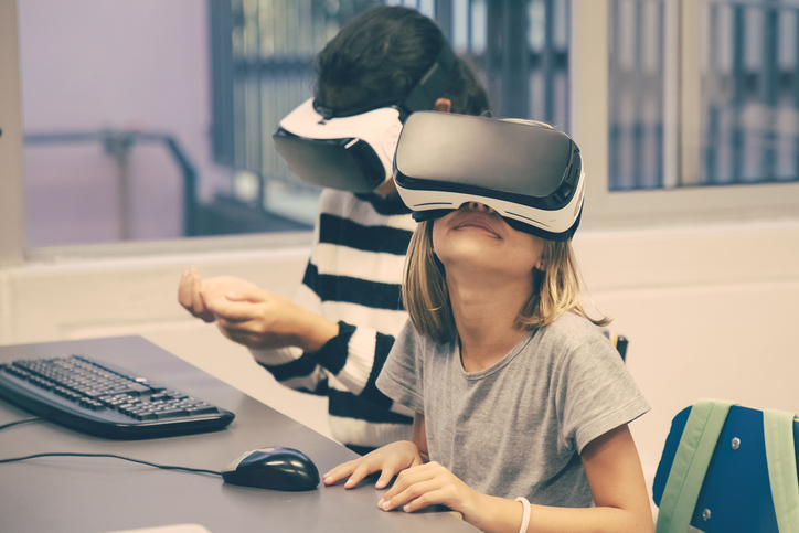 Criança em biblioteca sentada ao computador utilizando óculos de realidade virtual